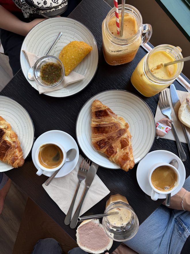 An overhead table of coffees, pastries and cold drinks with hands at the edges