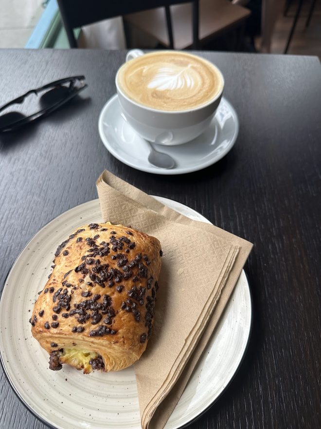 A latte and a chocolate-chip pastry on a dark table