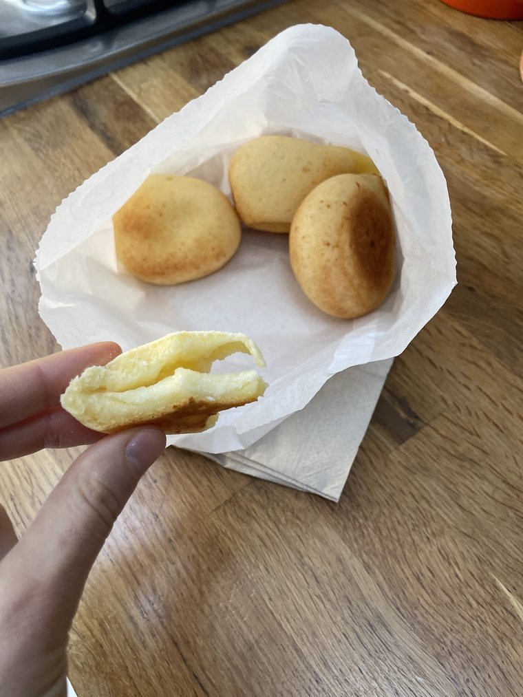 A split pandebono held above a paper wrap of two more